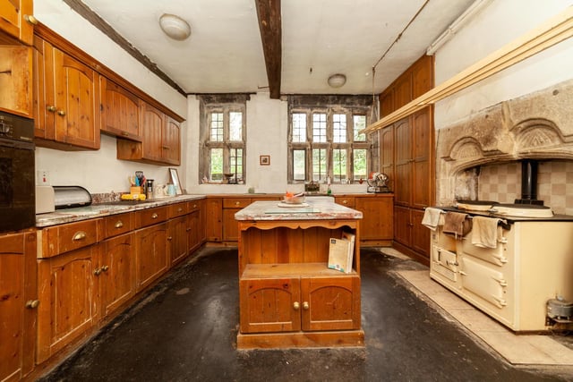 A central island is a feature of the kitchen, that has wooden panelling and ceiling beams.