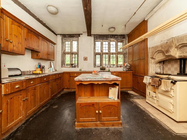 A central island is a feature of the kitchen, that has wooden panelling and ceiling beams.