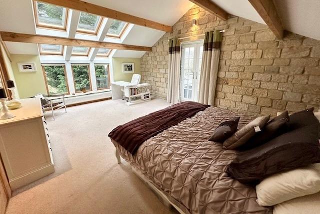 A bright and spacious bedroom with beams and exposed stone wall.