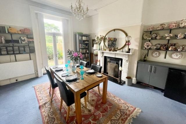 The dining room, with fitted shelving, has a period fireplace with open grate fire and French doors leading outside.
