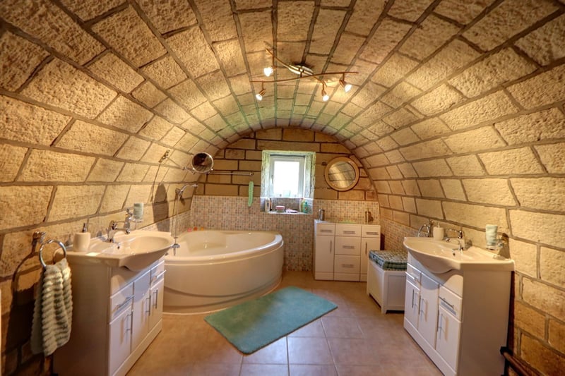 This stunning ground floor bathroom features an arched stone roof, and has a corner bath and twin vanity wash basins within its suite.
