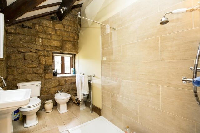 A walk-in shower features within this part tiled bathroom, with beams and stone wall.