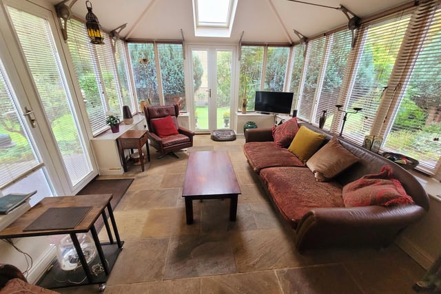 This conservatory has all-round views of the lawned and leafy garden with doors leading outside.