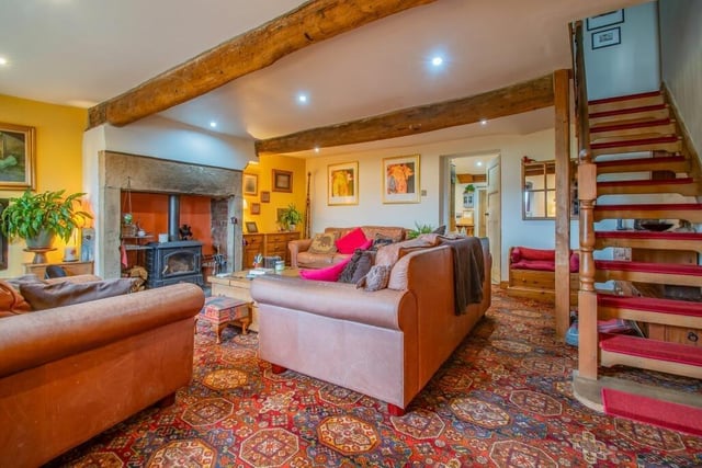 A rustic-style sitting room with overhead beams and a large feature fireplace with stove.