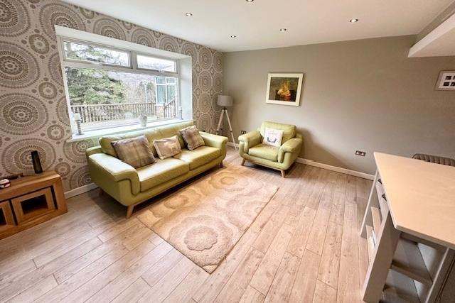 A bright family area has a wall-mounted tv and sound bar, with underfloor heating and mood lighting. French doors open to the garden.