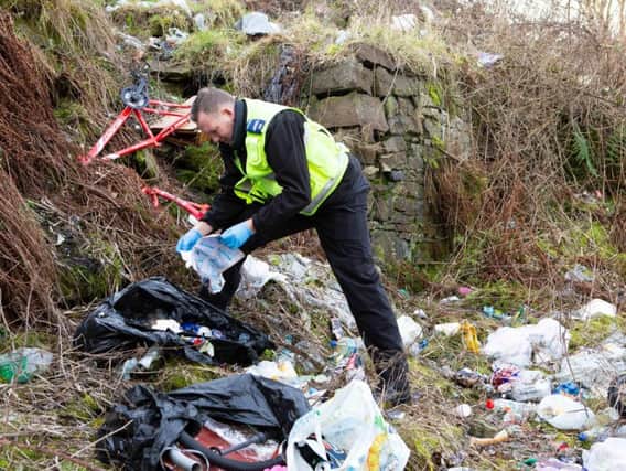 Community Safety Warden Craig Heywood, inspects rubbish at a fly tipping hot spot in Pellon